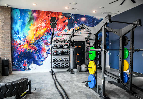 A gym with a large mural on the wall and various exercise equipment.
