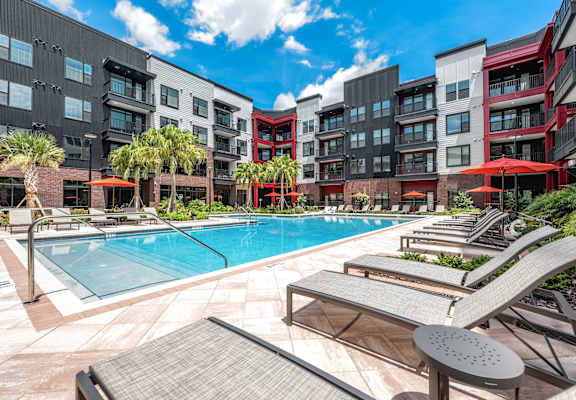 A pool surrounded by lounge chairs and umbrellas in front of apartment buildings.at Parkway Crossings, Kissimmee, 34744