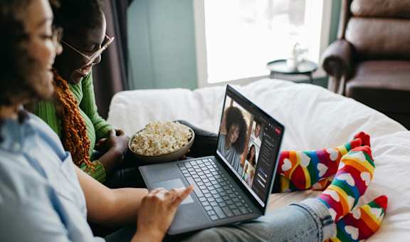 Two people are sitting on a bed with a laptop and a bowl of popcorn.