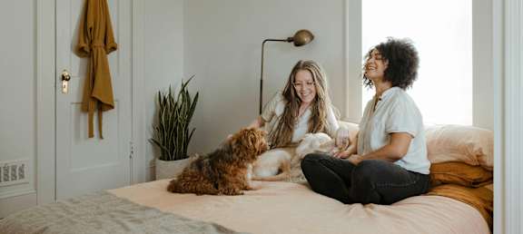 Two women sitting on a bed with a dog.