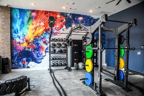 A gym with a large mural on the wall and various exercise equipment.