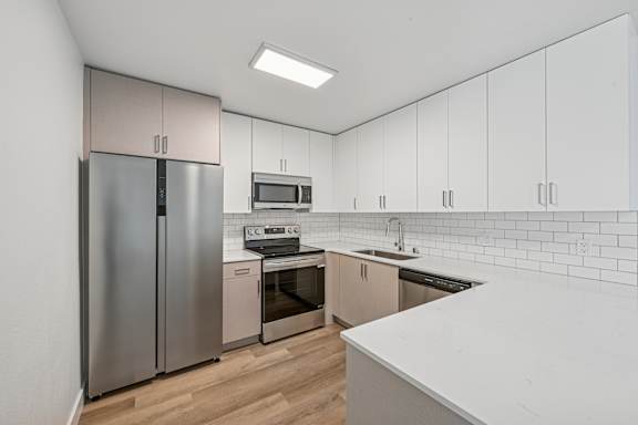 A kitchen with a refrigerator, microwave, oven, and sink.