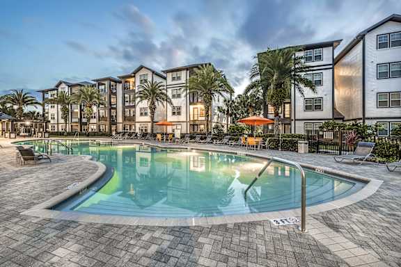 A large swimming pool surrounded by a brick patio and lounge chairs.