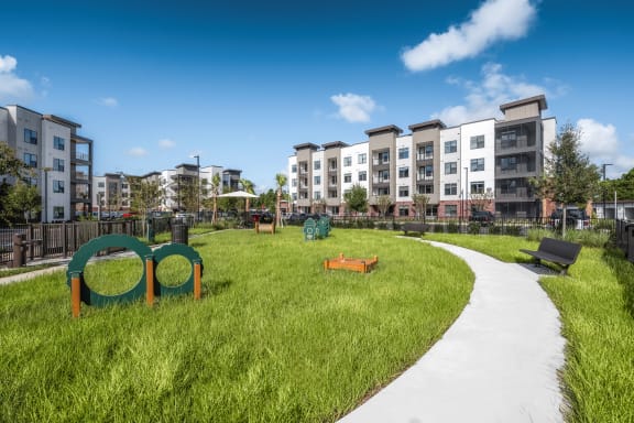 a park with green grass and a path with an apartment building in the background at The Haven at Lake Britt Apartments, Winter Garden, FL 34787