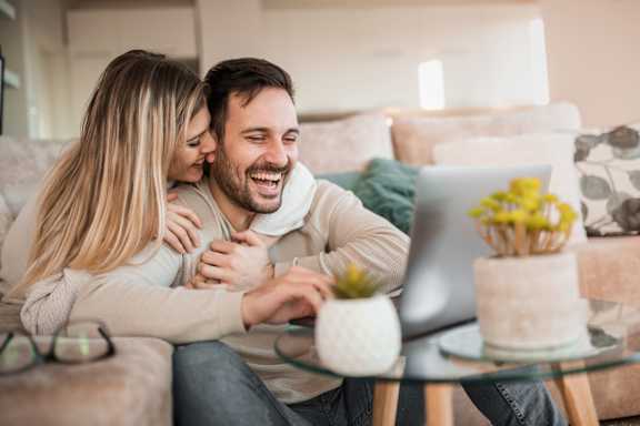 A man and woman are sitting on a couch with a laptop in front of them. at The Woodlands Apartments, Milton Keynes