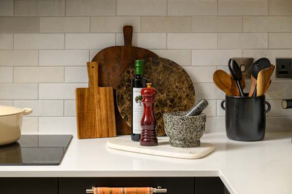 A kitchen counter with a cutting board, a bottle of red wine, a mortar and pestle, and a pot.