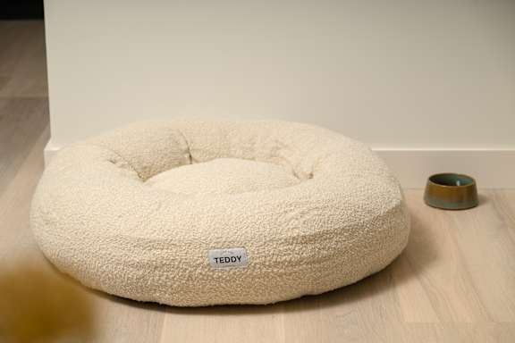 A white teddy bed with a small bowl beside it.