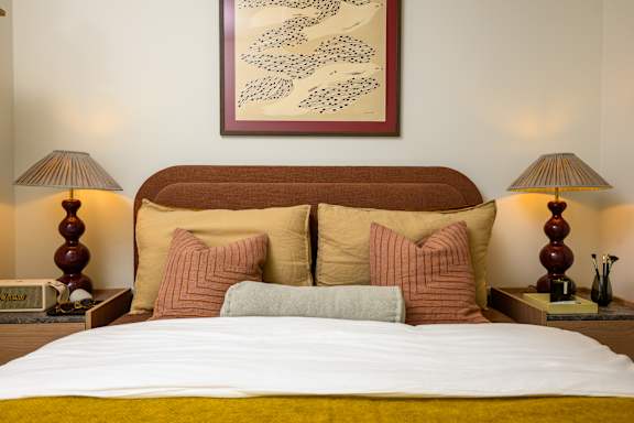 A bed with a white comforter and a yellow blanket is flanked by two lamps on either side.