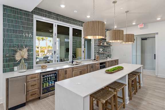 A kitchen with a long white island and wooden bar stools.