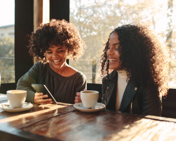 two women sitting at a table laughing while looking at a cell phone