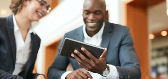 a man and a woman in business attire look at a tablet