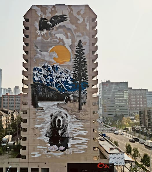 A large mural on a building features a bear, a wolf, a sunset, and a forest scene.