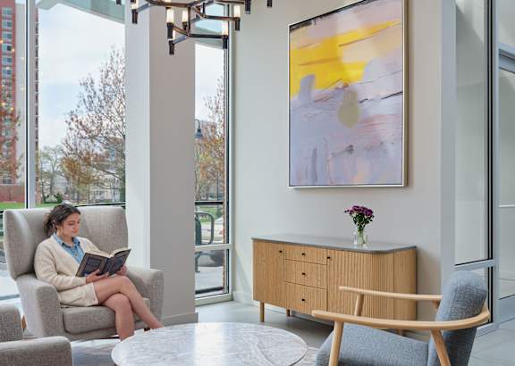 A woman is sitting in a chair reading a book in a well-furnished room.