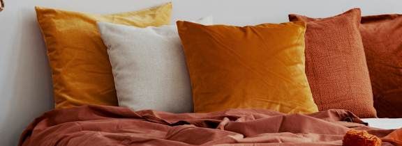 A bed with a brown comforter and pillows in shades of orange and brown.