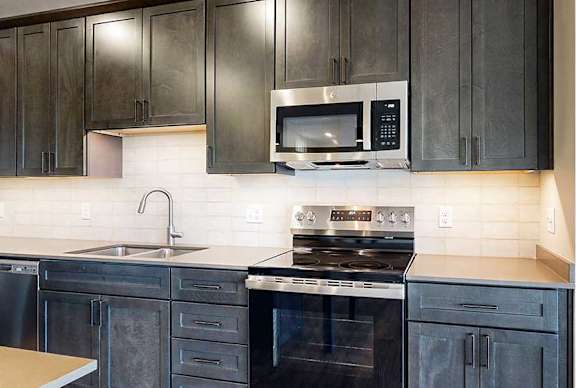 a modern kitchen with dark cabinets, a tile backsplash, quartz countertops, and stainless steel appliances