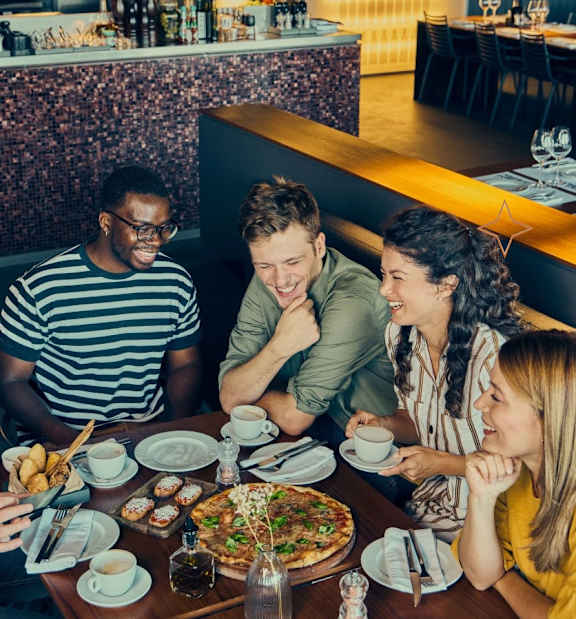 A group of people are sitting around a table with food and drinks.