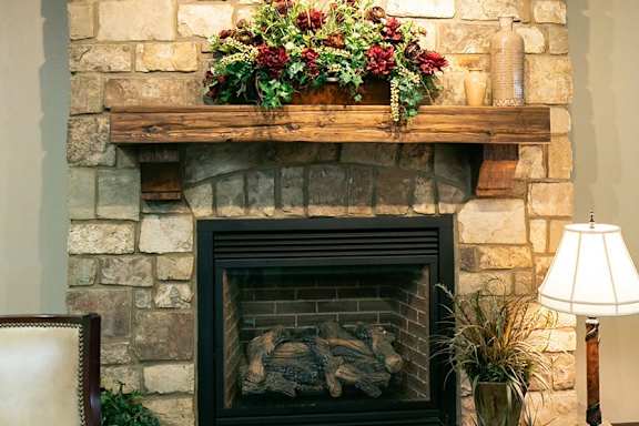 A stone fireplace with a wooden mantle and a plant on top.