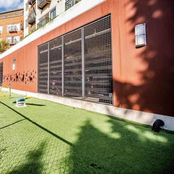 A small grassy area in front of a building with a fence on the left side.