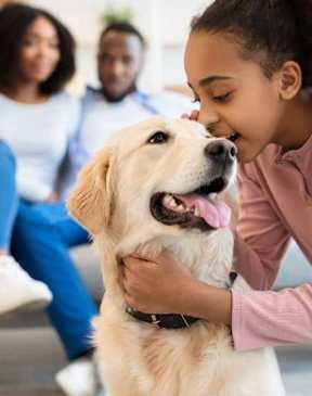 A young girl is kissing a dog on the cheek while two adults watch.