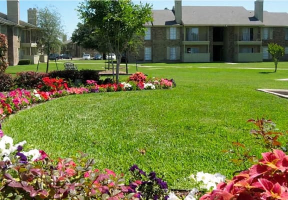 a lush green lawn with flowers in front of an apartment building  at Wymberly Pointe, Grand Prairie, TX, 75052