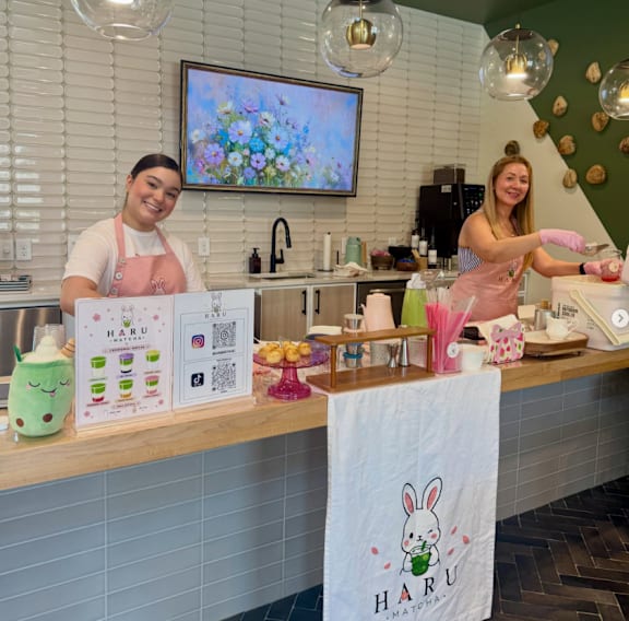 Two women working in a kitchen with a sign that says Haru.