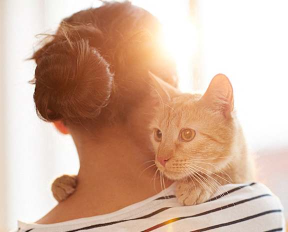 a woman holding a cat on her shoulders