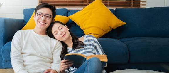 A man and woman are sitting on a blue couch, with the woman holding a book.