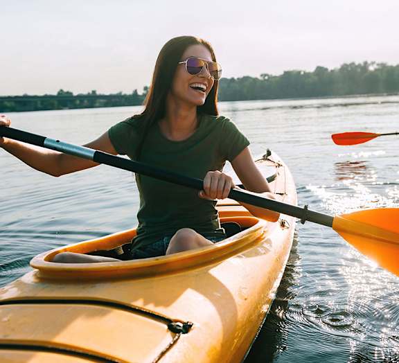 A woman is kayaking on a calm body of water.
