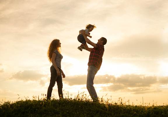 A family of three is silhouetted against a sunset sky.