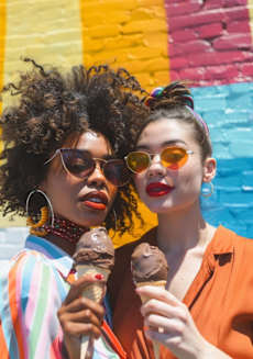 two women eating ice cream in front of a colorful wall