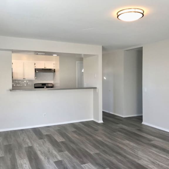 an empty living room with a kitchen in the background