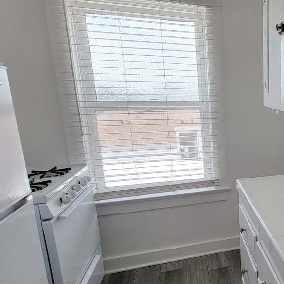 A white kitchen with a stove, sink, and window.
