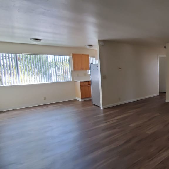 an empty living room with a kitchen in the background