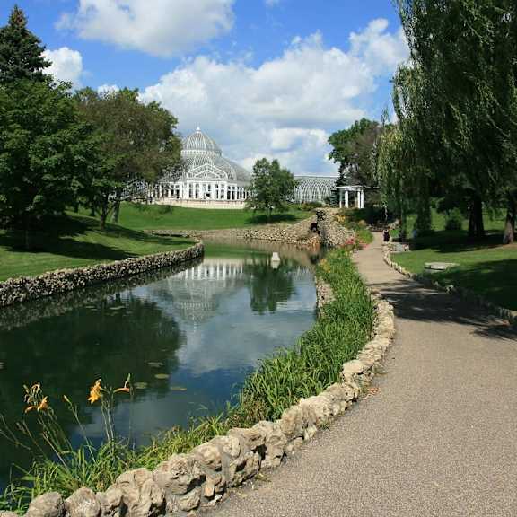 A serene park with a pond, a stone wall and a building in the background.