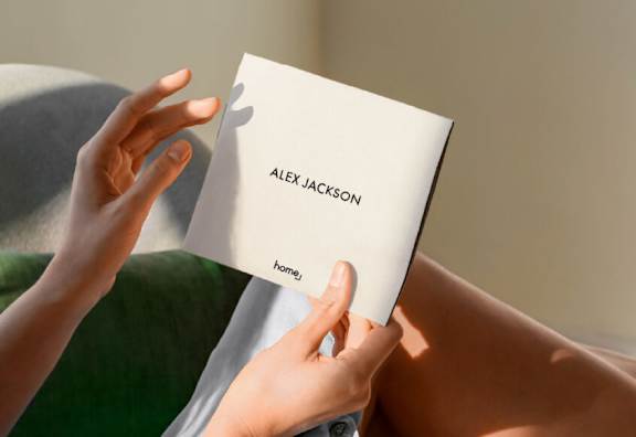 A person is holding a white card with the name "ALEX JACKSON" and the word "home" on it.
