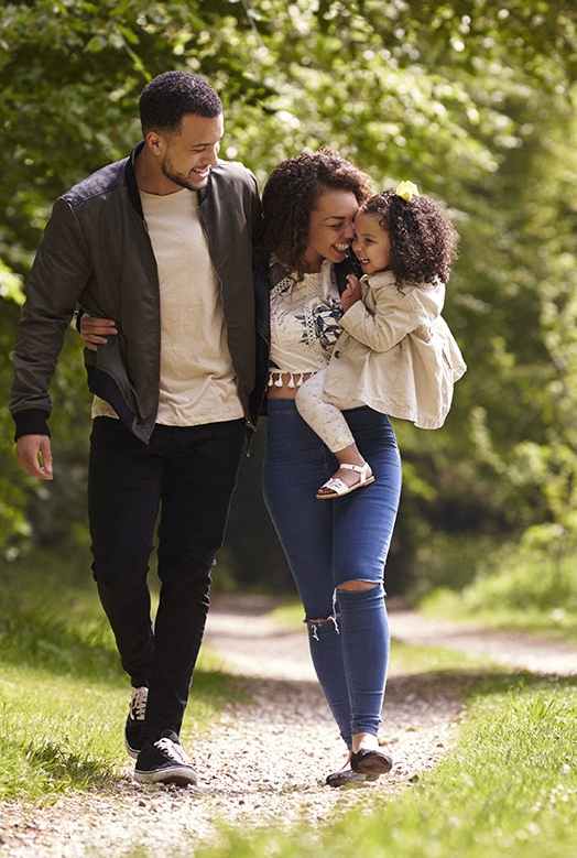 A family of three walking down a gravel road in a wooded area.