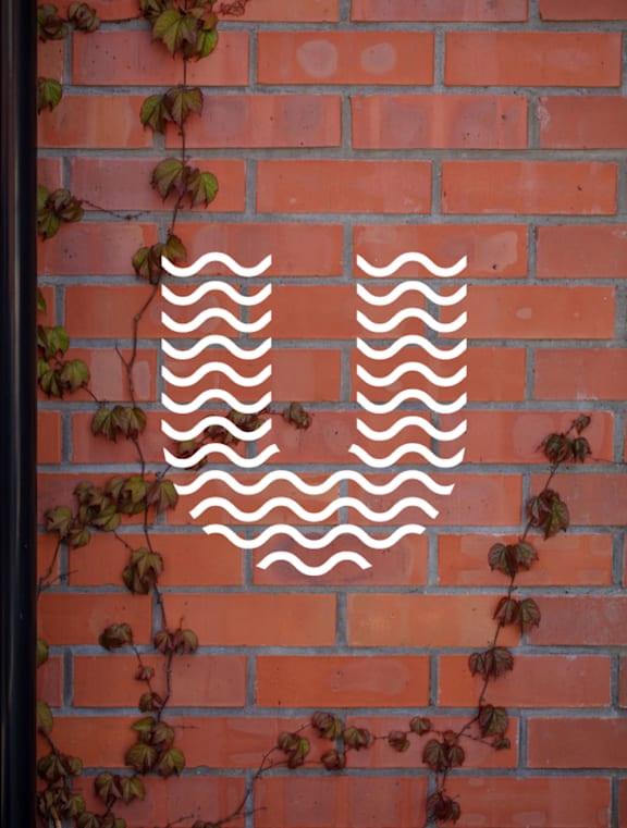 a logo on a brick wall with leaves on it