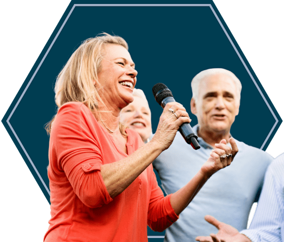 A woman in a red shirt is holding a microphone and appears to be speaking to an audience.