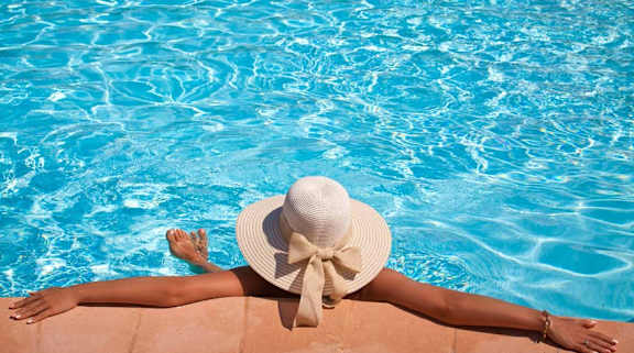 Woman in beach hat lounging peacefully in pool.