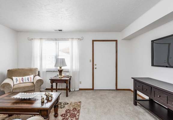 A living room with a couch, a coffee table, a lamp, a rug, a door, and a television.