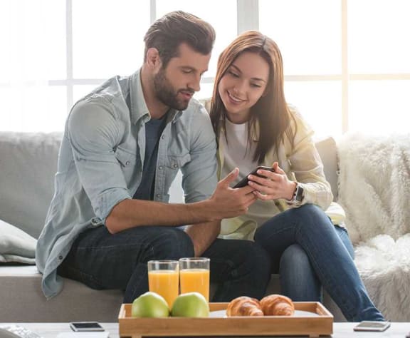 a man and woman sitting on a couch looking at a cell phone