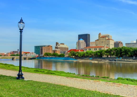 A cityscape with a river in the foreground and a clear blue sky above.