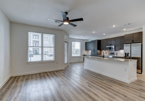 A spacious kitchen and living room with wooden floors and a ceiling fan.