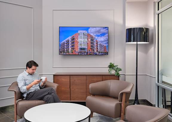A living room with a brown couch and a flat screen TV mounted on the wall.