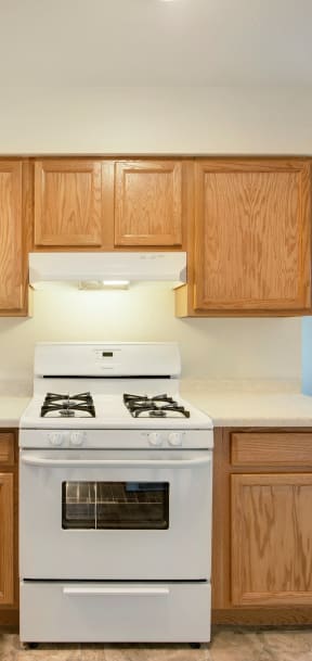 A white stove with a white oven in a kitchen with wooden cabinets. at Northeast Villas, Minnesota, 55421