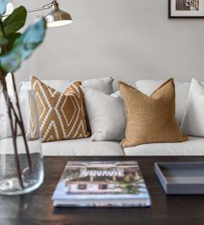 Living room with white couch, lamp, vase, and book on table at Appletree Apartments.