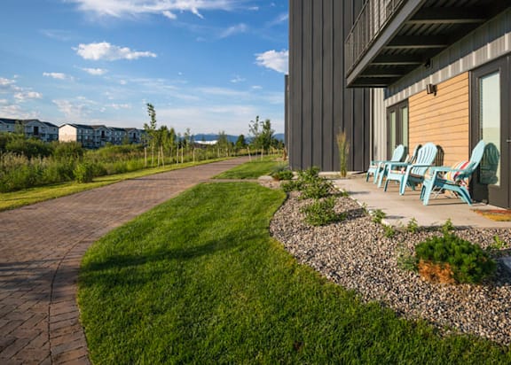 A patio area with a table and chairs is surrounded by a grassy area and a gravel path.