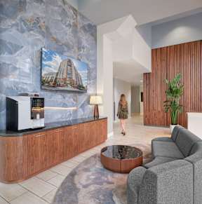 A woman walks through a modern lobby with a coffee machine on the counter.