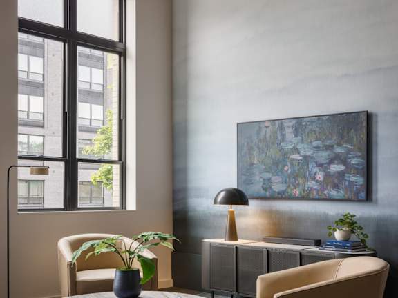 A living room with a large window, a round table with a plant on it, and two chairs.