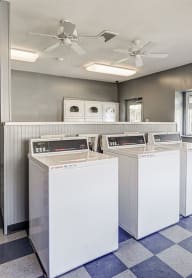 a laundry room with four washers and dryers on a checkered floor